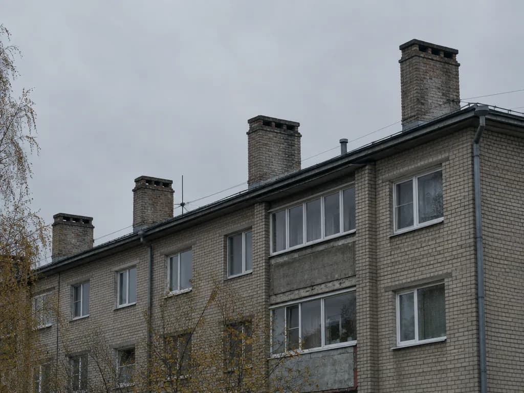 Nõukogudeaegse tellisest korterelamu katuseserv mitme korstnapiibuga, hall taevas